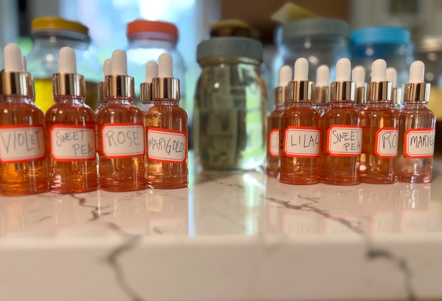 Dropper bottles of flower essences labelled violet, sweet pea, rose and marigold, on a marble counter