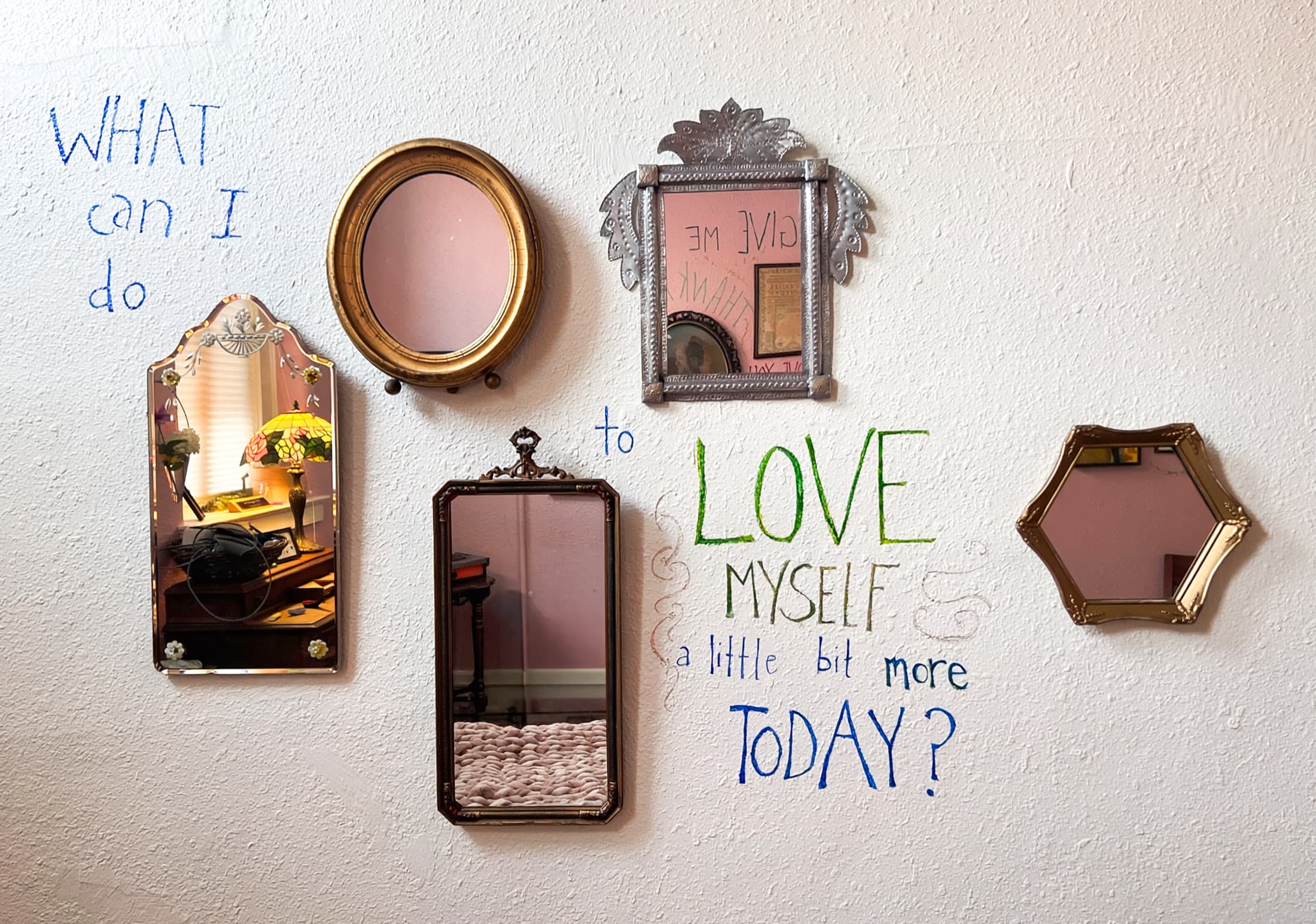 A wall of vintage mirrors, hand-lettered with the words: What can I do to love myself a little bit more today?