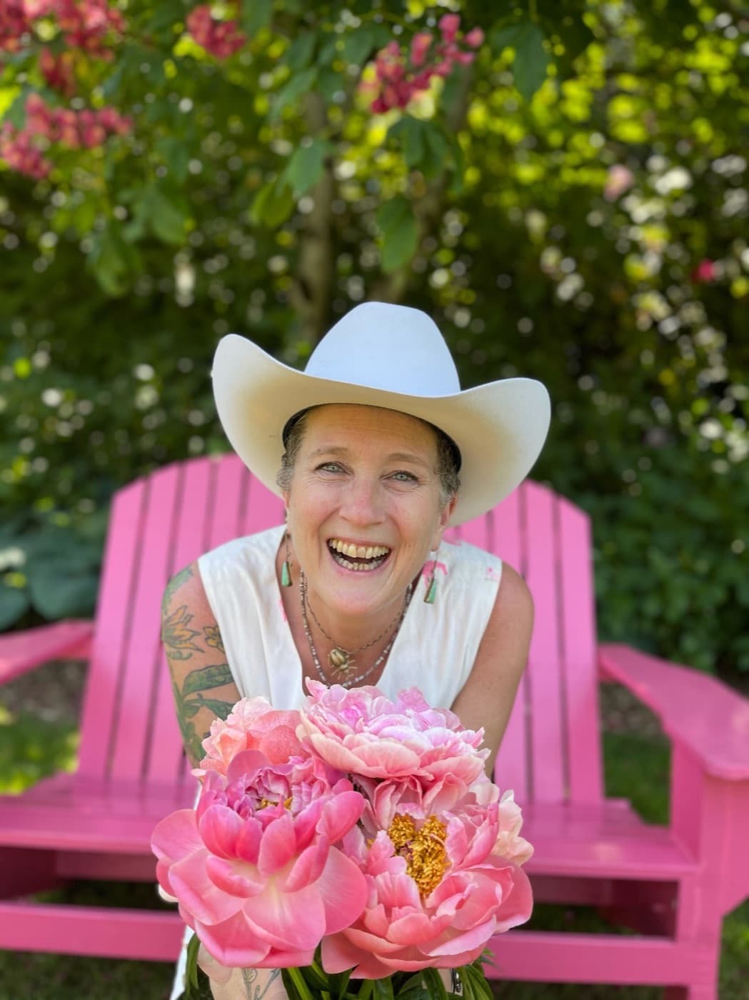 Dr. Rose laughing in a straw hat, holding an armful of pink peonies